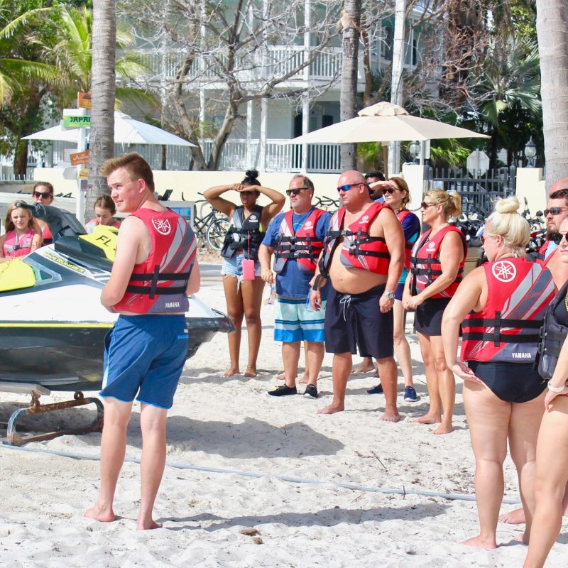 a group of people on a beach in life jackets ready to go on the Island Jet Ski Tour