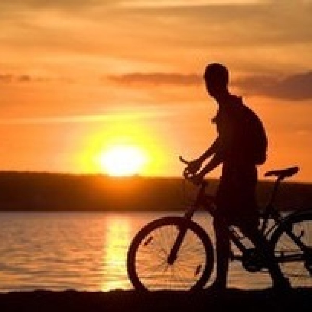 a man riding a bicycle with a sunset in the background