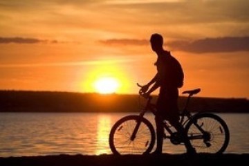 a man riding a bicycle with a sunset in the background