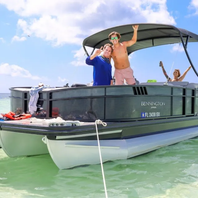 People enjoying a sunny day on a boat in clear, shallow water with blue skies.