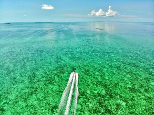 Aerial view of a boat speeding on clear turquoise water under a bright blue sky.