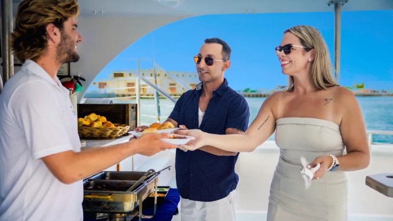 Couple on a boat receiving food from a server, clear sky in background.