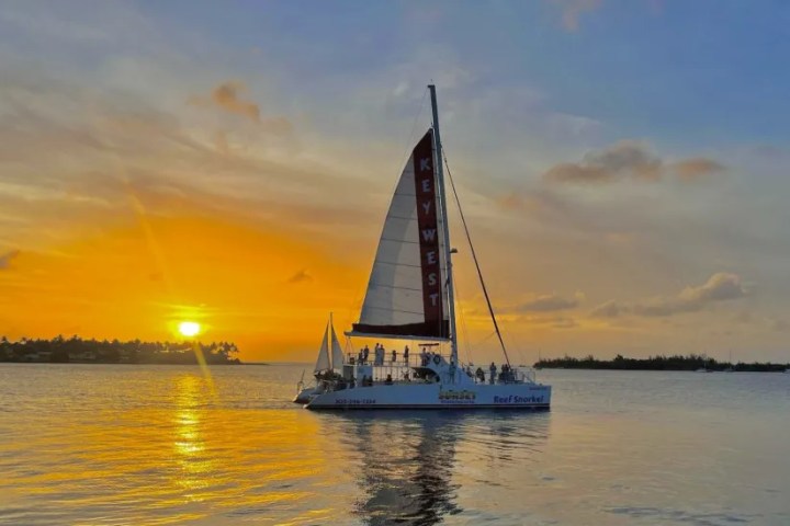 Sailboat at sunset with vibrant orange sky and calm water reflection.