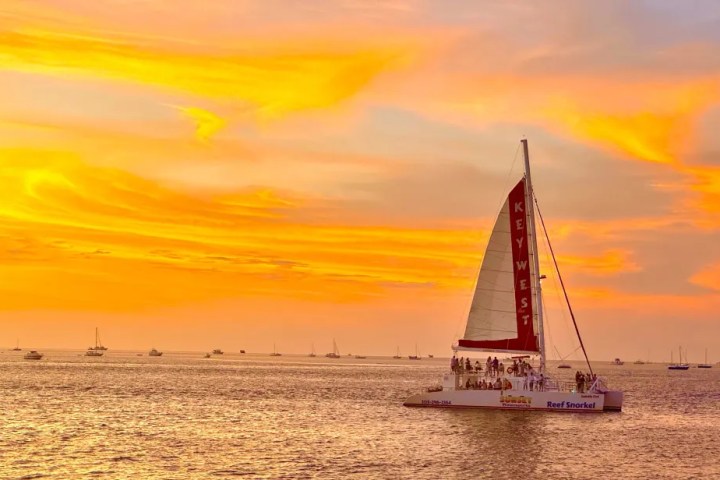 A sailboat on the ocean at sunset with orange skies and calm water, labeled 'Key West'.